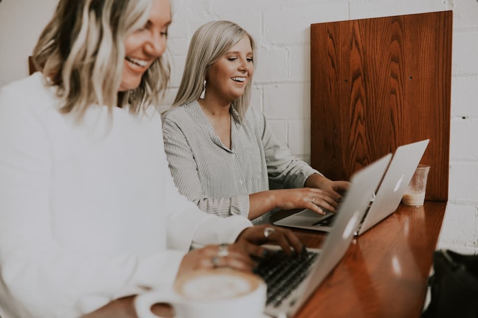Two women working on their laptops and laughing